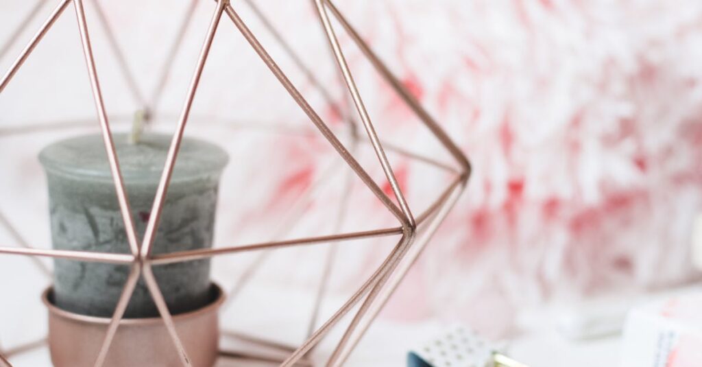 Rose gold geometric metal candle holder with a decorative candle inside, on a light background.